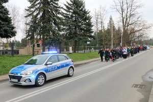 Policyjny radiowóz przed grupą uczestników drogi krzyżowej, w tle cmentarz miejski przy ul. Wyszyńskiego w Krośnie