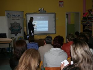 policjantka stojąca przy interaktywnej tablicy omawia uczestnikom prezentacje