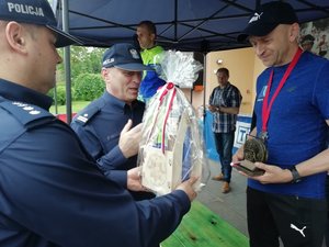 Kolorowa fotografia. Komendant Policji wręcza statuetkę i nagrody rzeczowe biegaczowi mundurowemu.