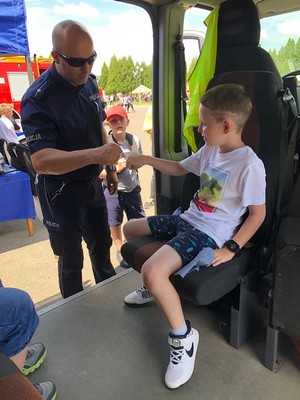 Policjant rozmawia z chłopcem, który siedzi w radiowozie policyjnym.