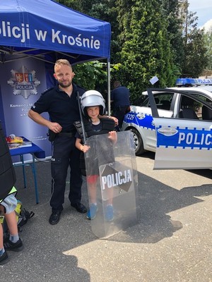 Policjant wraz z chłopcem, który przymierza umundurowanie policyjne wykorzystywane do zabezpieczania imprez masowych.