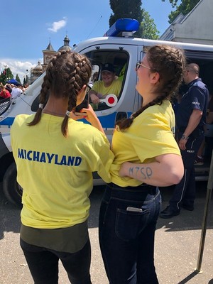 Na pierwszym planie uczestniczki Michaylandu 2019&quot;, które robią zdjęcie dziewczynce siedzącej w radiowozie policyjnym.