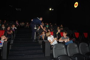 W sali kinowej policjant rozmawia z dziećmi.
