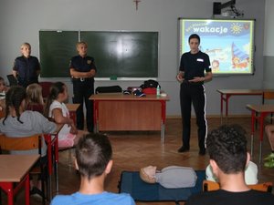 funkcjonariuszki straży miejskiej oraz policjantka przedstawiają w klasie lekcyjnej prezentację multimedialną na temat bezpiecznych wakacji
