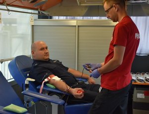 Zdjęcie przedstawia umundurowanego policjanta, który w obecności pielęgniarza oddaje krew.
