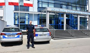 Zdjęcie przedstawia funkcjonariusza na tle radiowozów i budynku KPP Jarosław.