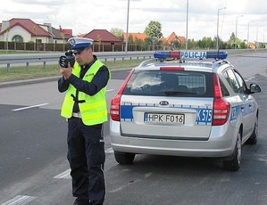 Na zdjęciu policjant mierzący prędkość, w tle radiowóz
