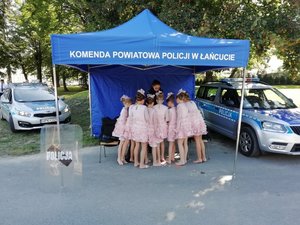 Namiot z napisem Komenda Powiatowa Policji w Łańcucie. Pod zadaszeniem przy policyjnym stoisku policjantka rozmawia z dziewczynkami z tanecznego zespołu Iskierka.