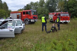 Fotografia przedstawia miejsce ćwiczeń zarządzania kryzysowego w Laszkach. Na zdjęciu widać radiowóz, wozy strażackie, policjantów i strażaków.