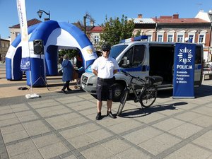 na fotografii funkcjonariusz w umundurowaniu policjanta z patrolu rowerowego, w tle radiowóz i rower policyjny na rynku starego miasta w Mielcu
