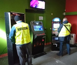 Na zdjęciu widoczni są funkcjonariusze w kamizelkach przy automatach do gier hazardowych