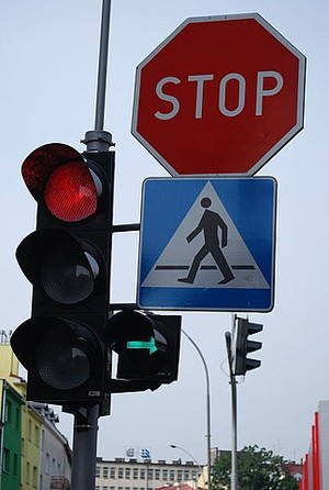 Na zdjęciu sygnalizator świetlny, znak STOP i znak wskazujący na przejście dla pieszych.