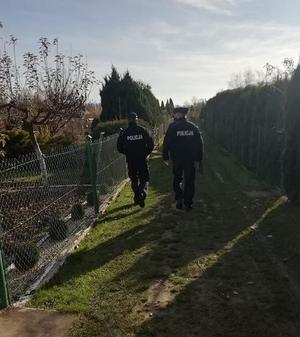 Na zdjęciu dwóch policjantów patrolujących ogródki działkowe.