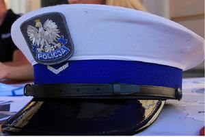zdjęcie kolorowe przedstawia czapkę policyjna (policjanta ruchu drogowego). z daszkiem oraz białym pokrowcem oraz niebieskim otokiem na środku którego znajduje się dystynkcja w kształcie litery v (stopień sierżanta).