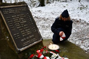 Złożenie kwiatów i zapalenie zniczy przy obelisku upamiętniającym katastrofę śmigłowca w Cisnej przez policjantów. Policjantka zapala znicz.