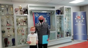 Komendant Miejski Policji w Krośnie z nagrodzonym w konkursie chłopcem na tle sztandaru krośnieńskiej Policji