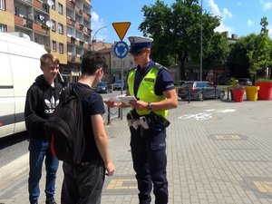 policjant ruchu drogowego przekazuje ulotki młodym chłopcom w rejonie przejścia dla pieszych