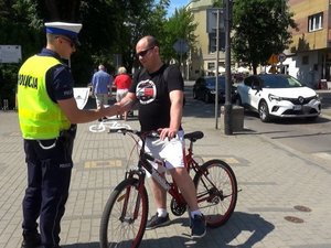 policjant ruchu drogowego przekazuje ulotkę informacyjno-edukacyjną rowerzyście