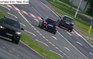 Zdjęcie z policyjnego wideorejestratora. Na zdjęciu trzy pojazdy osobowe, jedno z aut zaznaczone biało-czerwonym krzyżykiem. W lewym górnym rogu zdjęcia napis na białym tle, na pierwszym miejscu - dozwolona prędkość 50 km/h, następnie prędkość z jaką jechał kierowca oznaczonego krzyżykiem auta - 142 km/h