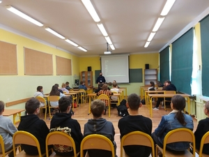 Na zdjęciu znajduje się policjant w sali szkolnej oraz grupa uczniów