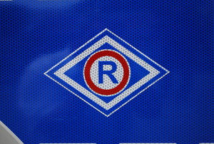 Oznaczenie służby ruchu drogowego, duża litera R wpisana w niebiesko-biały romb na granatowym tle.