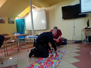 Umundurowany policjant uczestniczący w praktycznym szkoleniu pierwszej pomocy. Czynności wykonywane na podłodze z udziałem manekina.