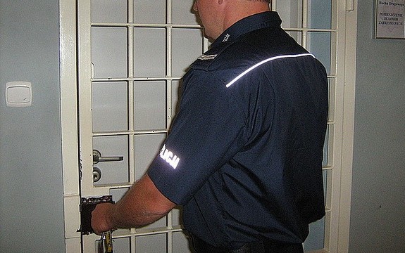Umundurowany policjant zamykający kraty od pomieszczenia dla osób zatrzymanych.