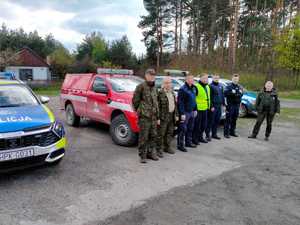 Wspólne zdjęcie biorących udział w działaniu funkcjonariuszy straży leśnej oraz policjantów. Stoją oni przed dwma radiowozami oraz pojazdami straży leśnej.
