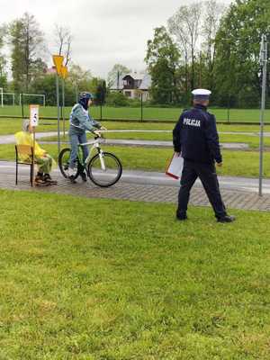 Na zdjęciu osoby biorące udział w turnieju ruchu drogowego. Rowerzysta jadący jednośladem przed nim umundurowany policjant.