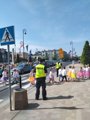 Policjanci stoją w rejonie przejścia dla pieszych, przez które przechodzą maluchy