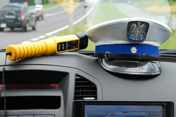 Na zdjęciu wewnątrz radiowozu widoczna jest czapka policjanta ruchu drogowego oraz żółty alkomat